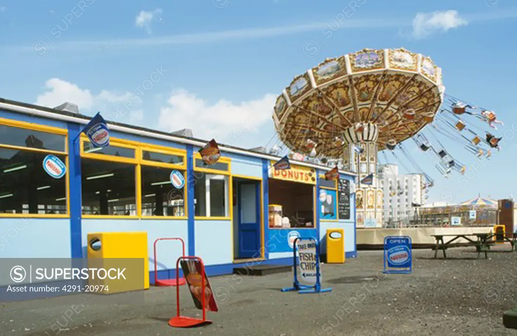 Yellow and blue fish & chip cafe in front of circular fairground attraction at Folkestone in Kent