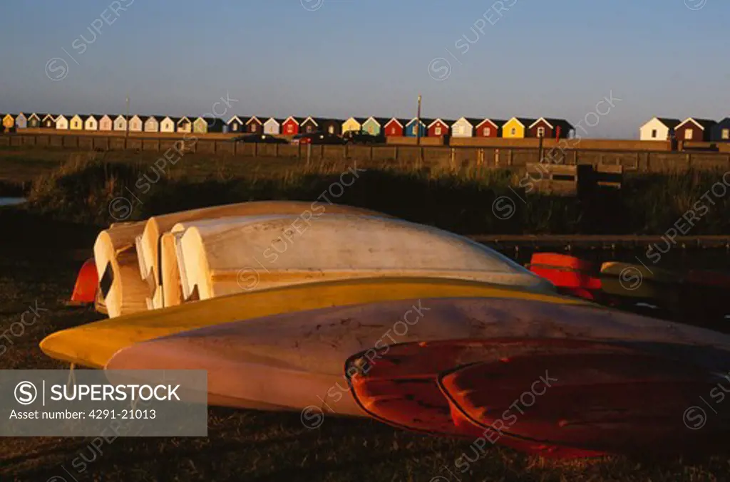 Upturned kayaks and boats on the beach with colourful beach huts in background at Southwold in Suffolk
