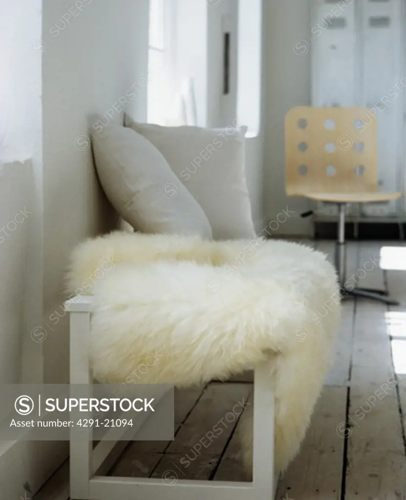 Close-up of cream sheepskin throw on white bench with grey cushions in city living room