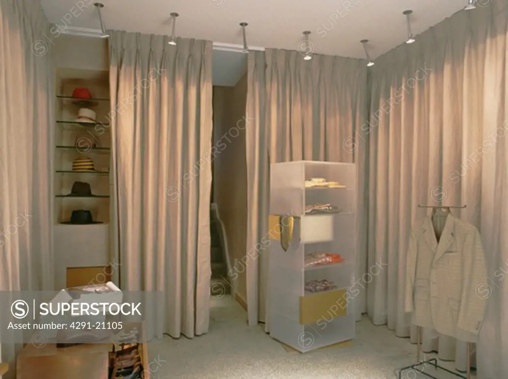 Spotlights above perspex shelving and beige curtains concealing storage
