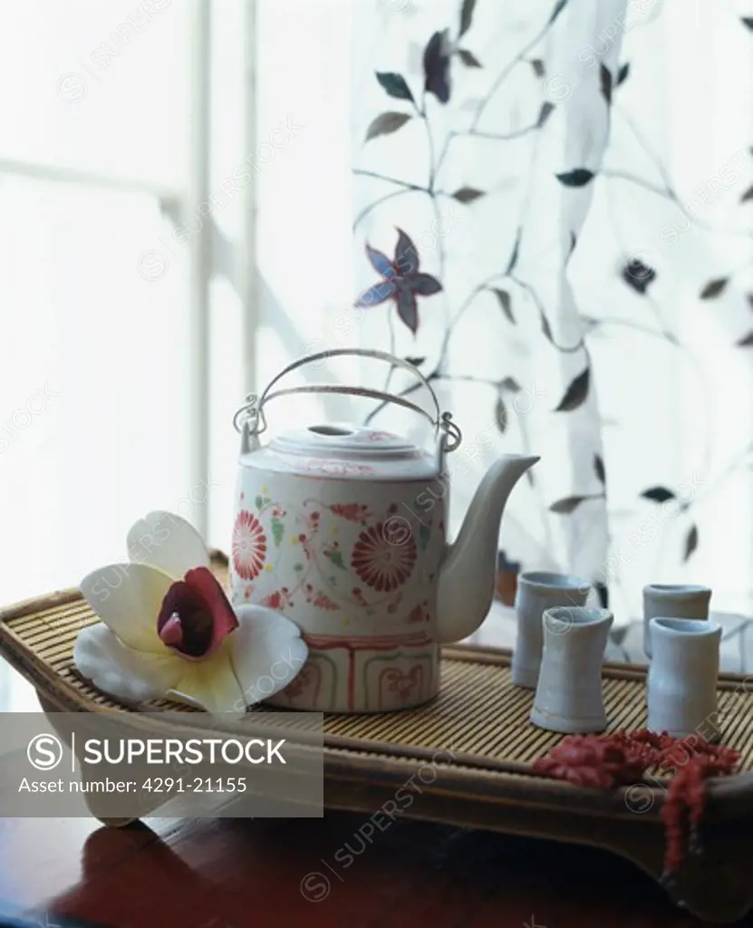 Close-up of oriental teapot and cups with orchid on bamboo tray