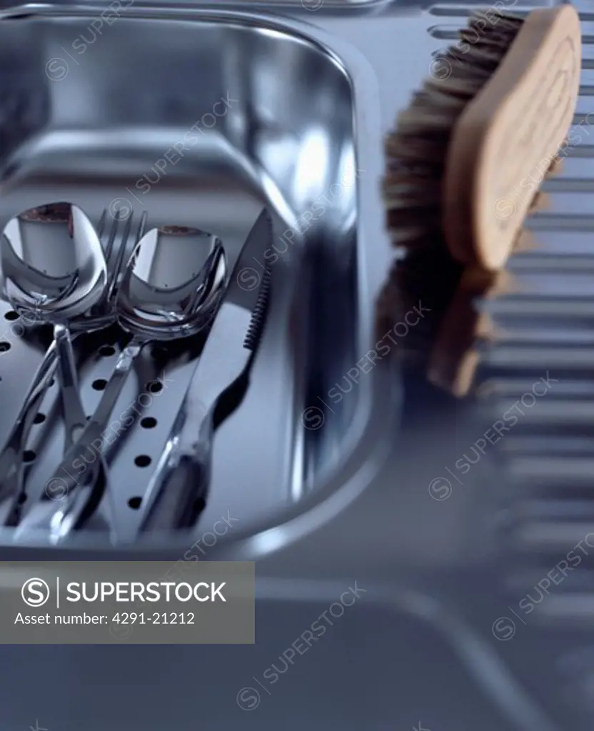 Close-up of scrubbing brush and stainless steel cutlery in stainless steel sink