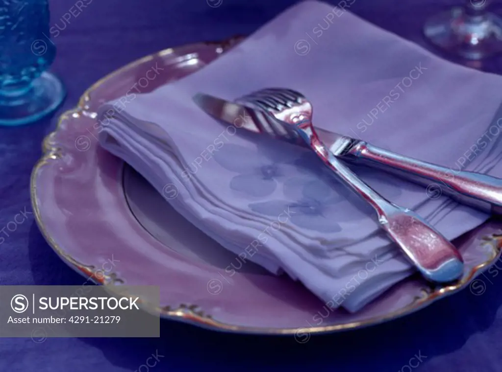 Close-up of silver cutlery and mauve napkin on purple plate