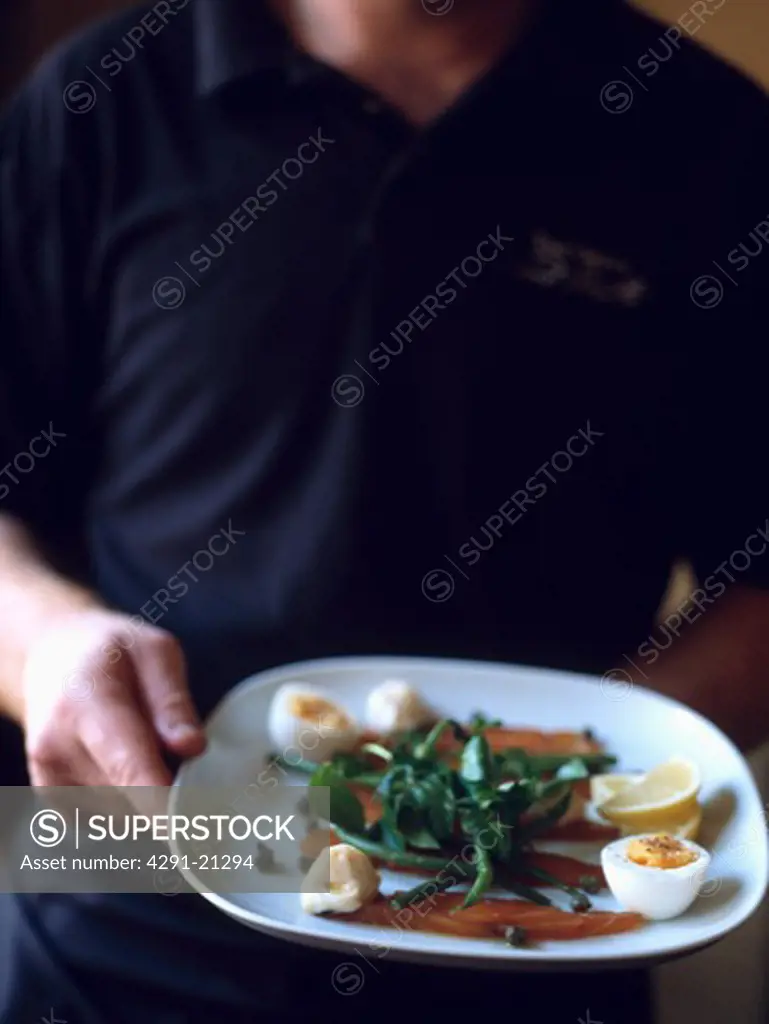 Close-up of waiter's hand with plate of smoked salmon and boiled eggs with green beans