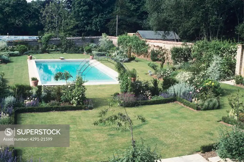 Lawn with formal flowerbeds and swimming pool in large country garden in summer