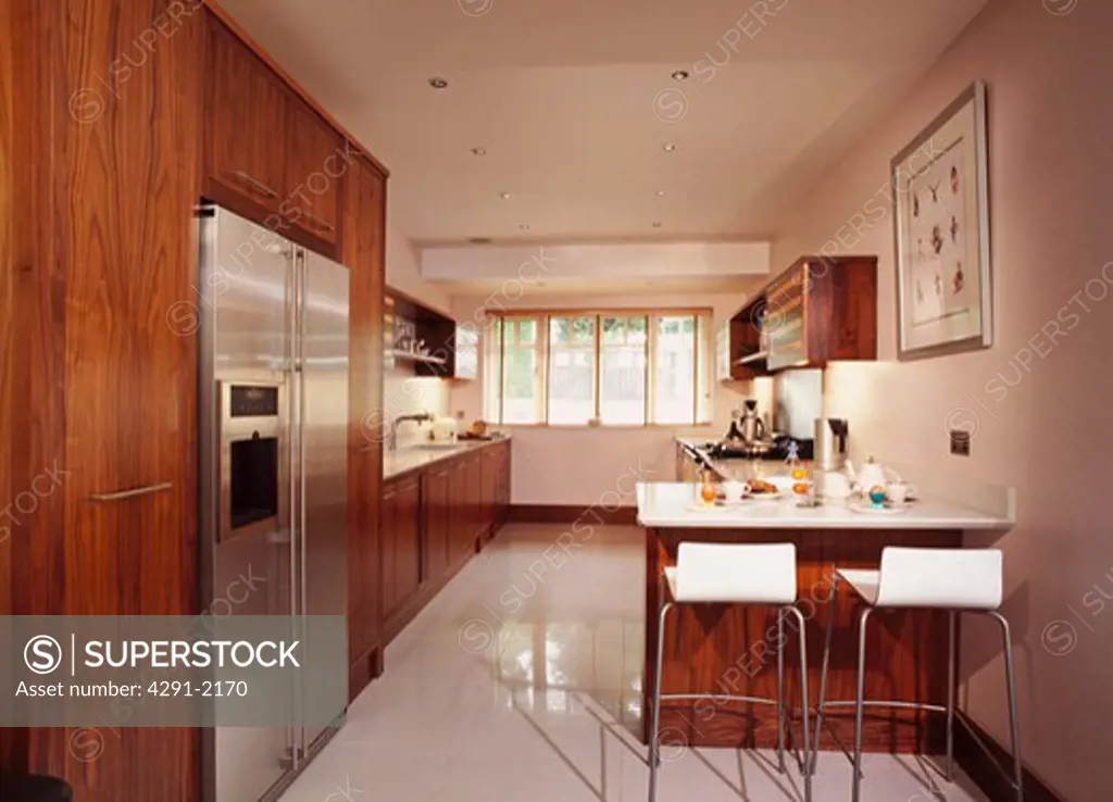 White stools at breakfast bar in modern kitchen with American style fridge freezer and white floor tiles