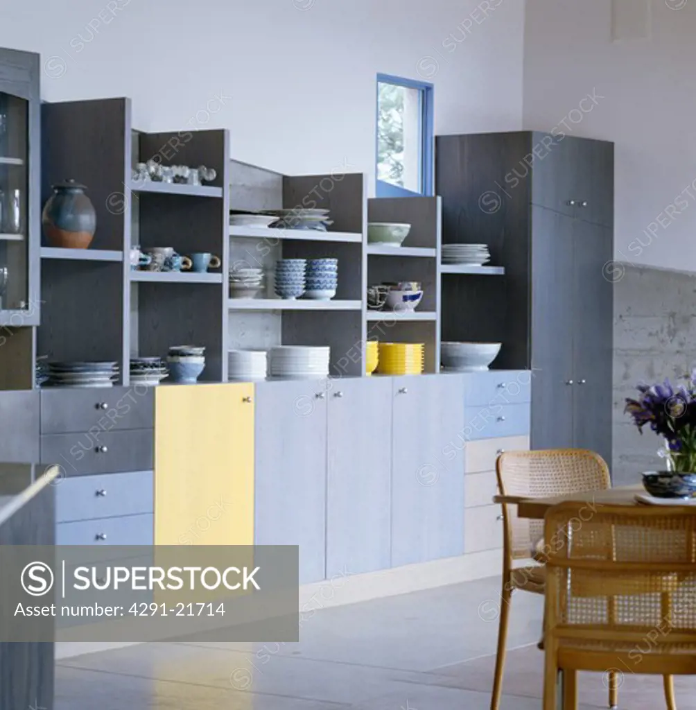 Crockery on open shelves in modern kitchen with pale blue fitted units