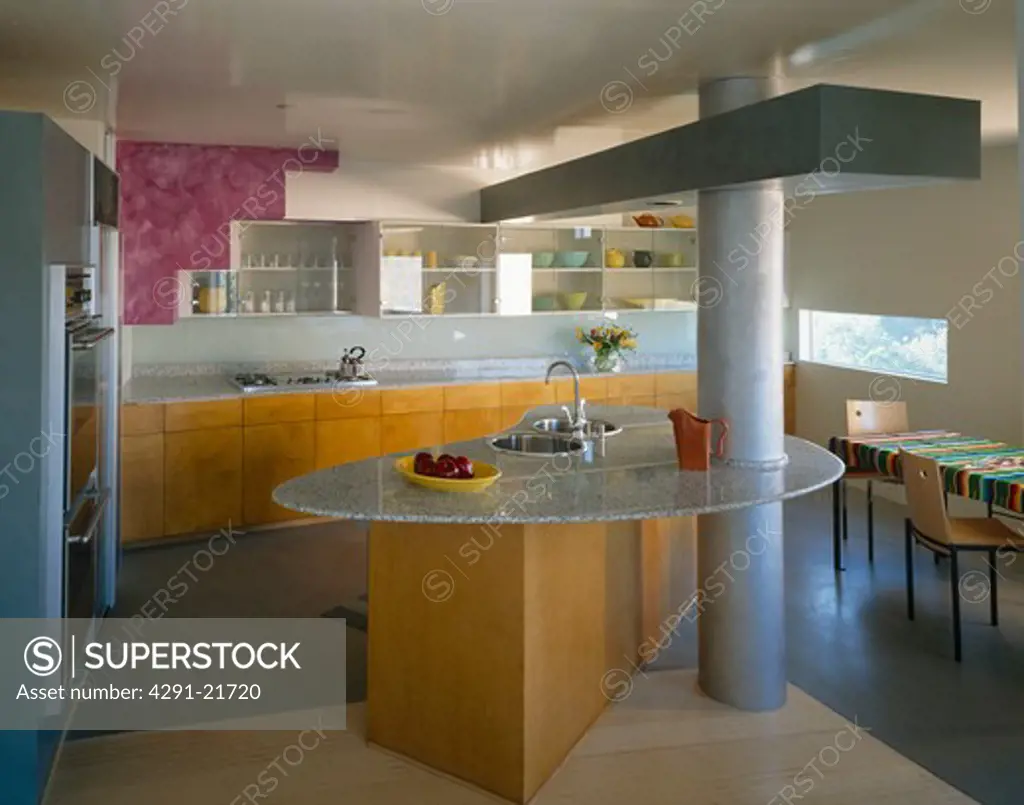 Low-ceilinged modern openplan kitchen with boomerang-shaped island with two sinks in granite worktop