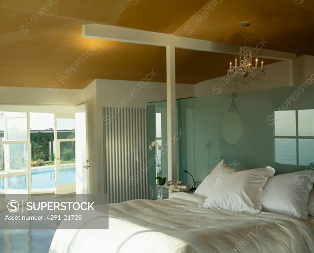 White bedlinen on bed in modern bedroom with glass doors open to swimming pool