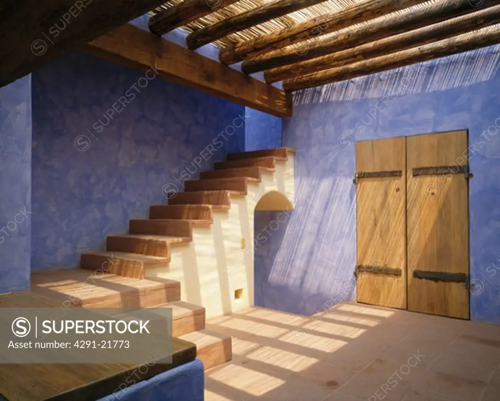 Textured blue walls in Mexican style hall with open staircase and wooden beams