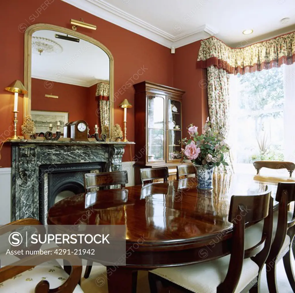 Antique mahogany table and chairs in red dining room with gilt mirror above black marble fireplace