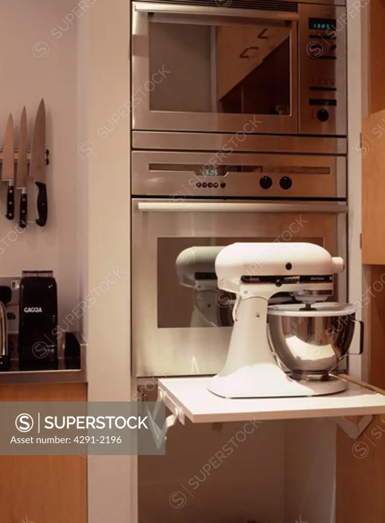Close-up of white Kitchenaid mixer on retractable shelf in front of double stainless steel oven