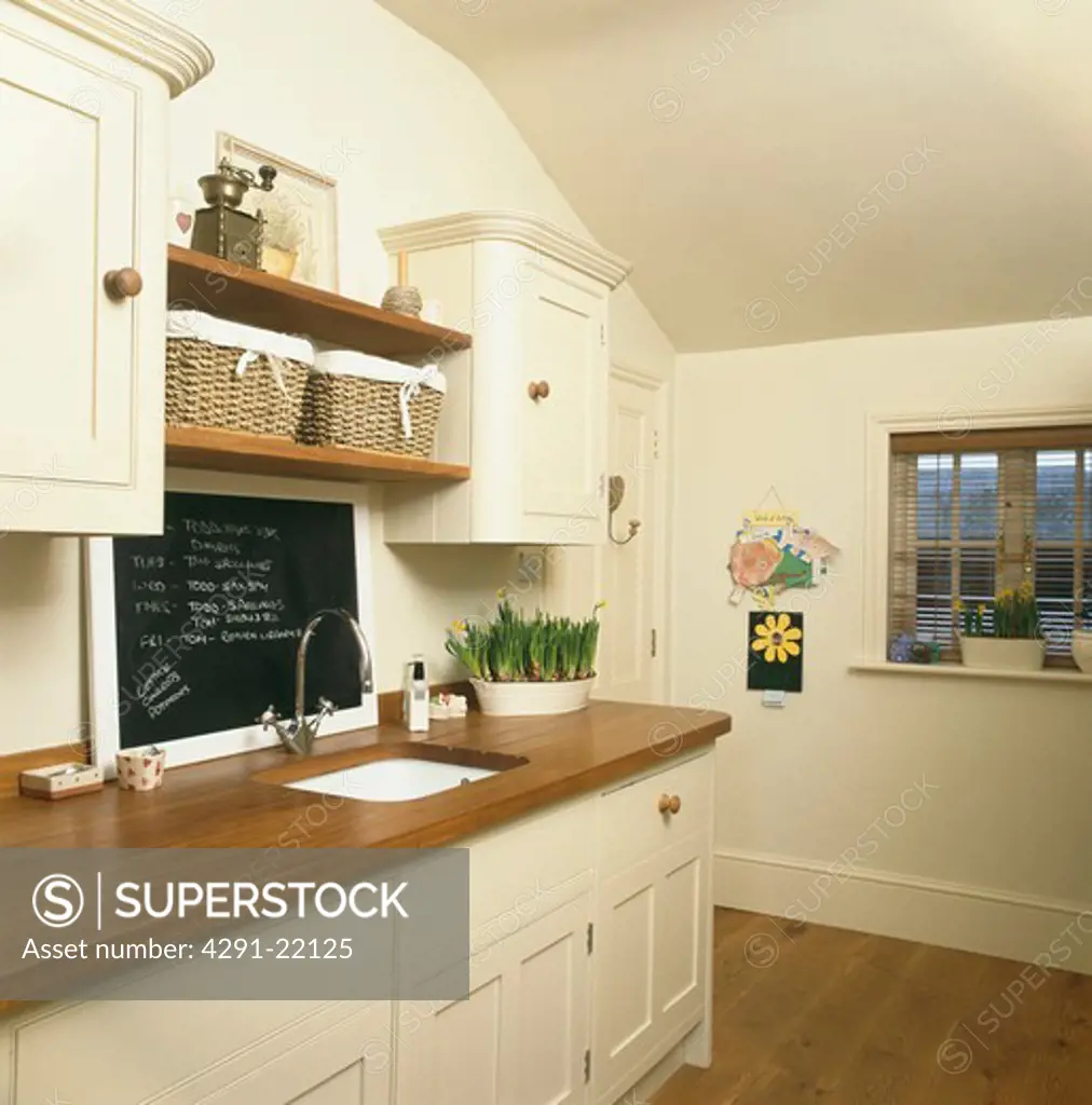 Blackboard above sink in wooden worktop in cream kitchen
