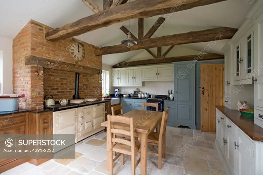 Reclaimed antique stone flooring and wooden table and chairs in kitchen with cream Aga in Tudor brick fireplace