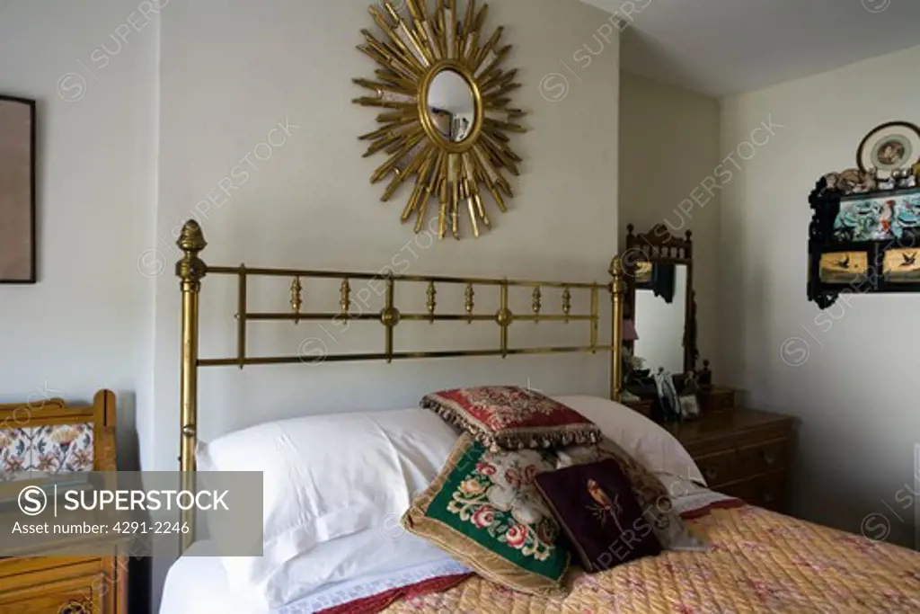 Starburst mirror above antique brass bed with white pillows and tapestry cushions in traditional bedroom
