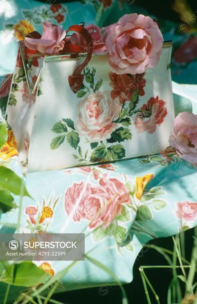 Still-life of pink roses in rose-patterned handbag on rose-print fabric