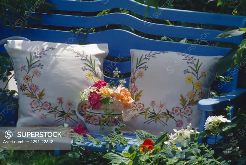 Still-life of roses and embroidered cushions on blue garden bench