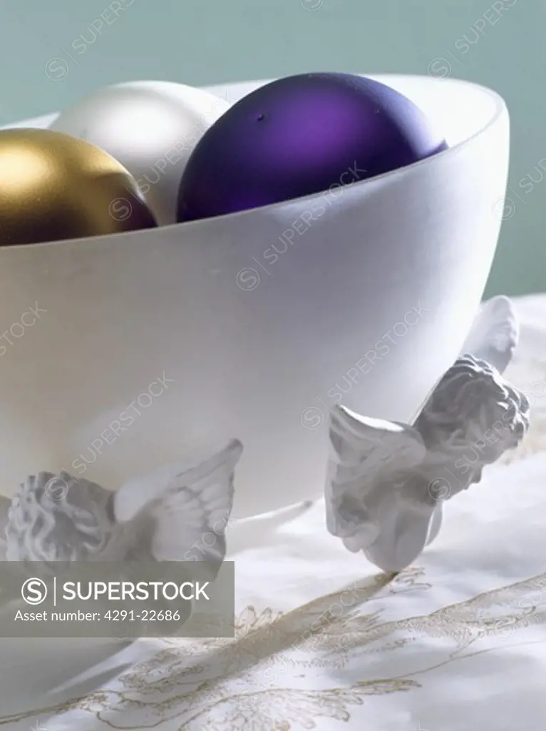 Detail of frosted glass bowl with cherub feet containing Christmas baubles
