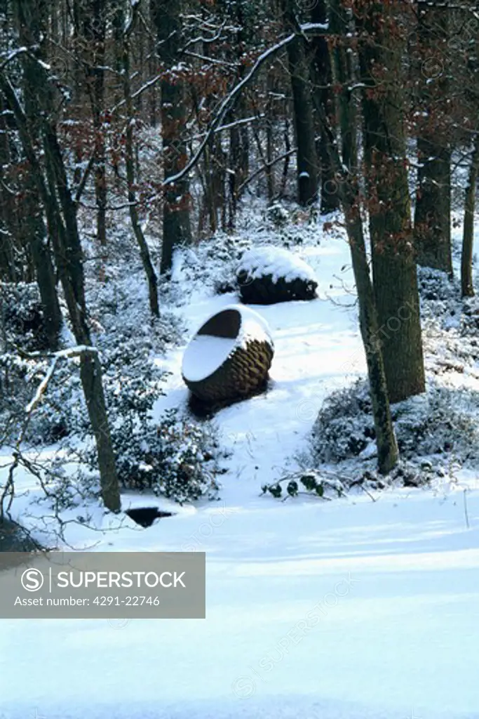 Snow in woodland garden with sculpture in winter