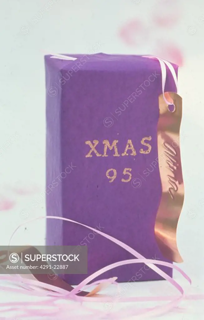 Close-up of Christmas present wrapped in gold paper and decorated with gold lettering and copper gift tag