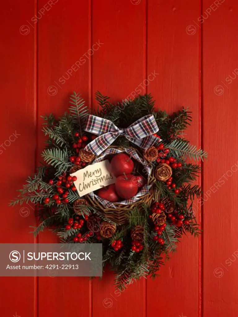 Close-up of red apple and berry and green conifer wreath tied with tartan ribbon