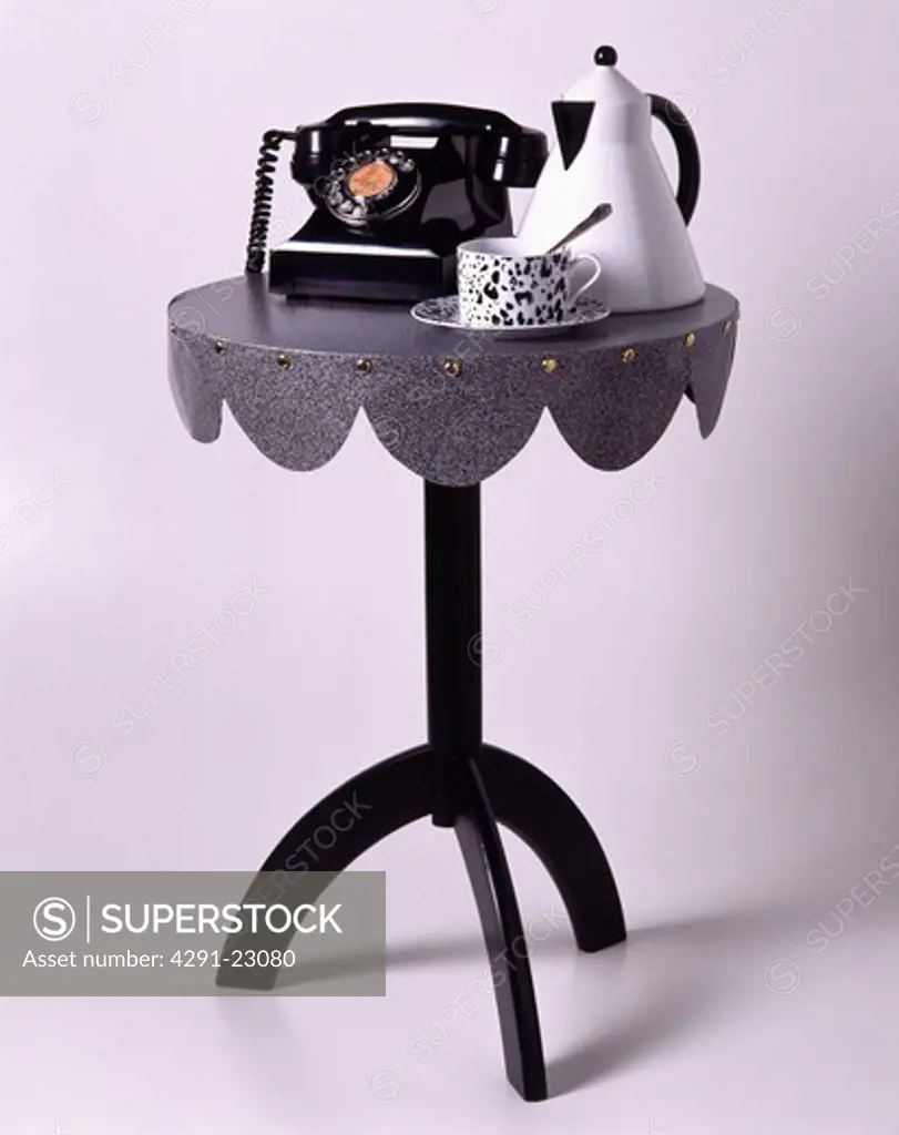 Close-up of retro telephone on black metal table with white coffee-pot and black and white animal-print cup