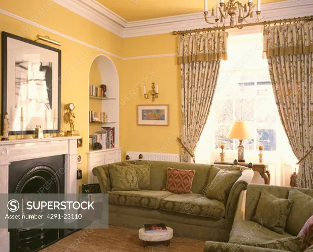 Patterned curtains and green sofas beside fireplace in yellow livingroom