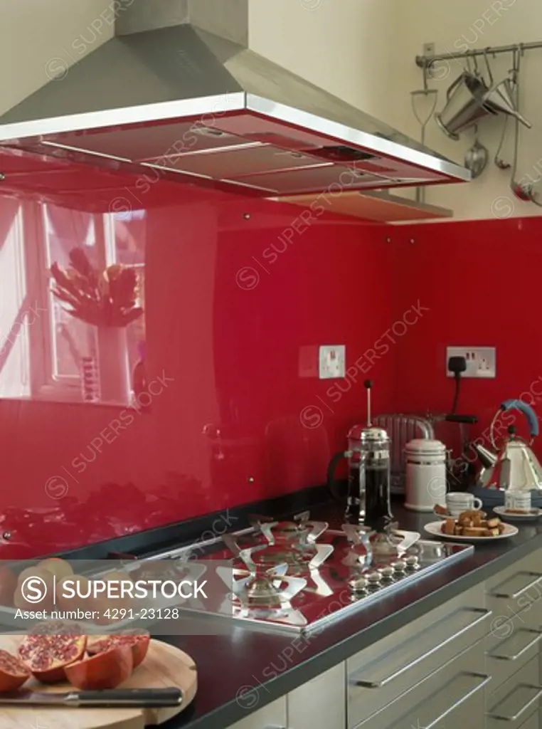 Close-up of gas hob below stainless steel extractor fan in modern kitchen with red glass panels