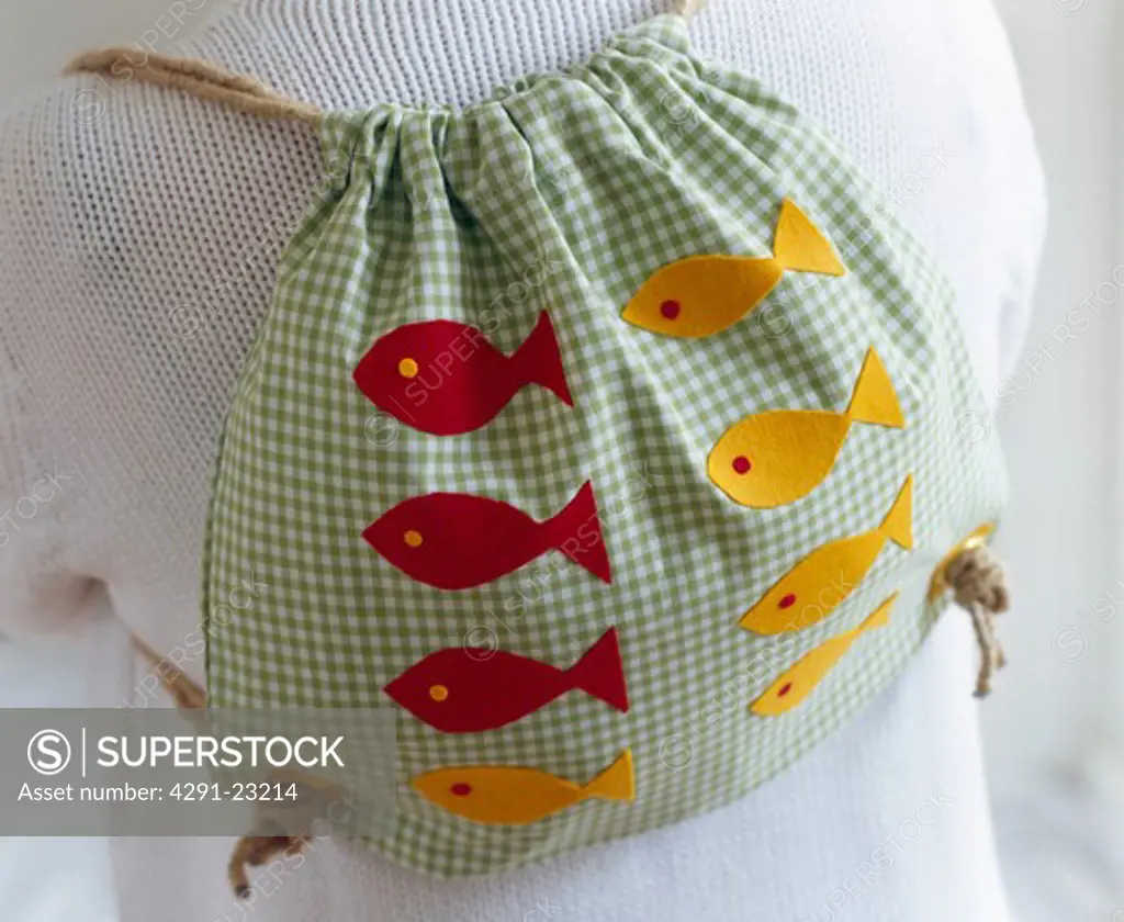 Close-up of person wearing green check cotton rucksack appliqued with red and yellow fish