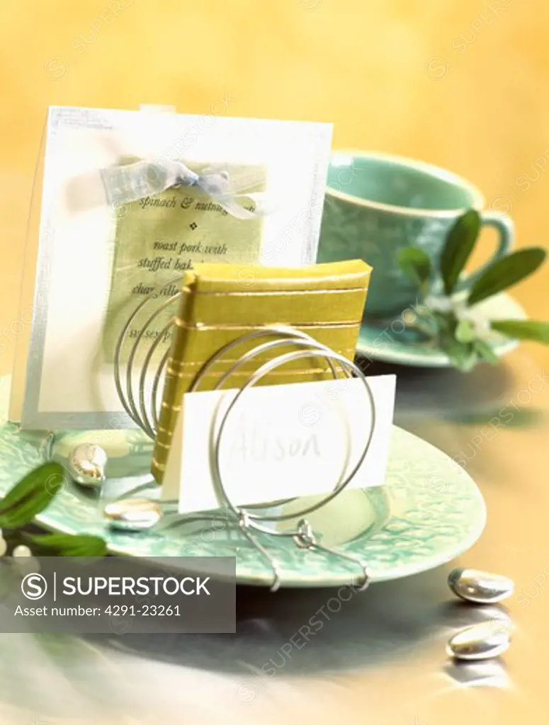Close-up of hand-made place-card and small yellow notebook in wire holder on green plate with menu card