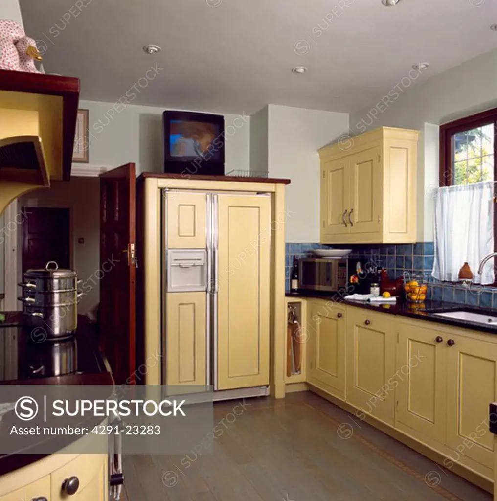 Flatscreen television above large fridge-freezer in cream kitchen with wooden flooring