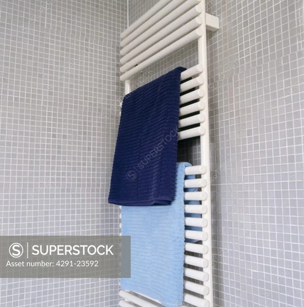 Blue towels on white heated towel rail on grey mosaic tiled bathroom wall