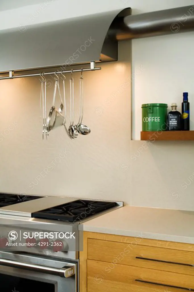 Lighting above tainless steel utensils on rack above steel range oven in modern kitchen