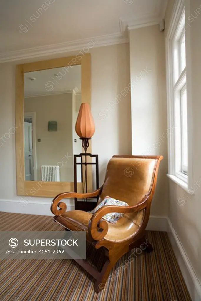 Antique beige leather and wood armchair on cream landing with large mirror on wall and striped carpet
