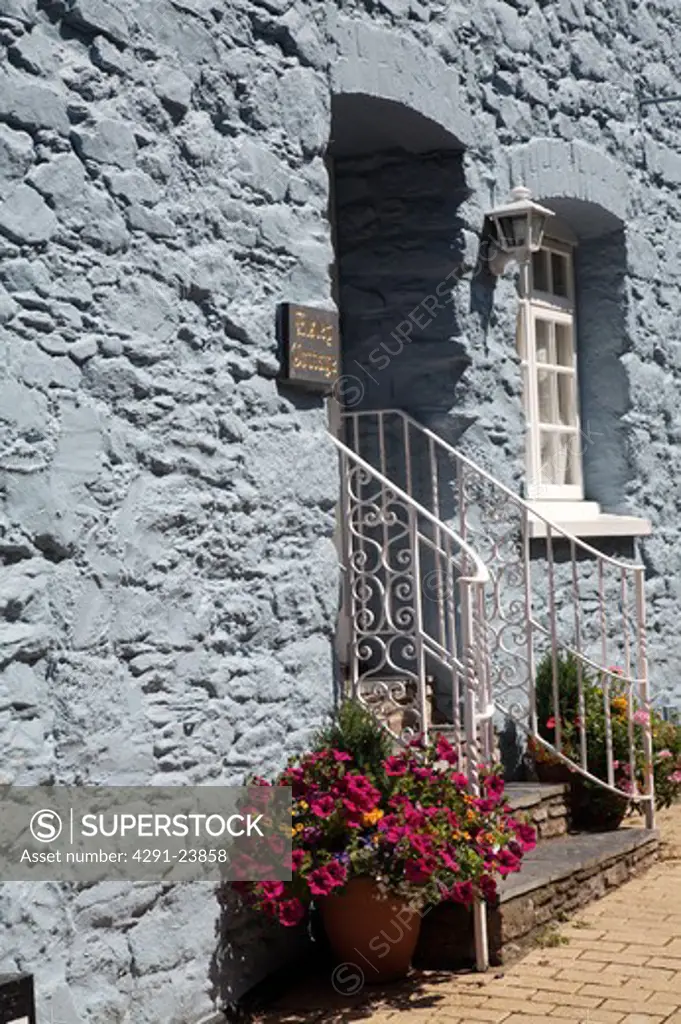 Grey painted stone cottage with white iron handrails on either side of steps