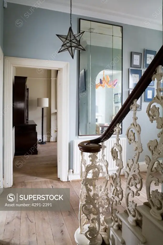 Stained oak handrail and ornate iron balusters in grey hall with engineered oak floorboards and large antique mirror