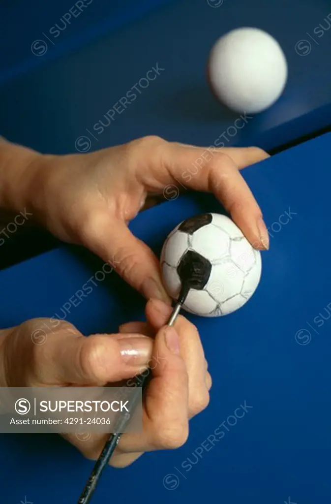Close-up of hand painting small white ping-pong ball to resemble football
