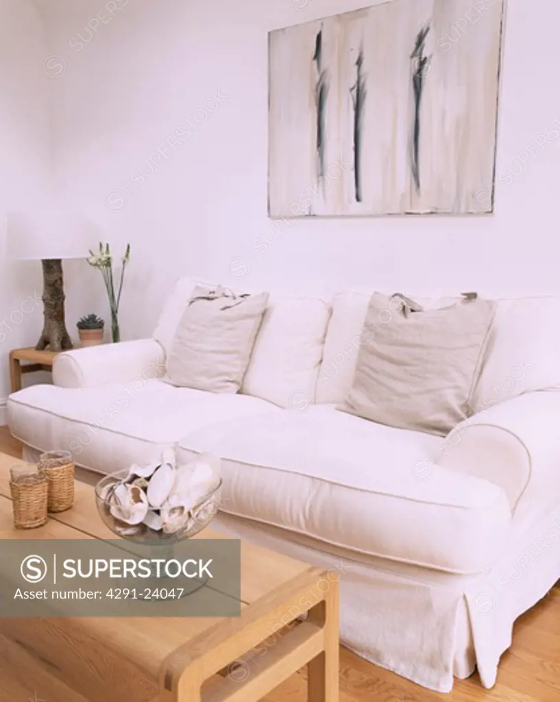 Abstract picture above white sofa with loosecover and grey cushions in modern white living room