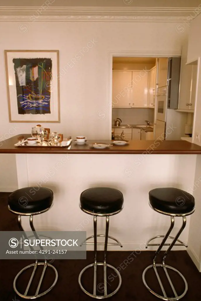 Black leather and chrome stools at breakfast bar in modern white kitchen