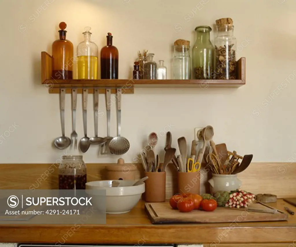 Glass bottles on wooden shelf above wooden worktop with utensils in pottery jars