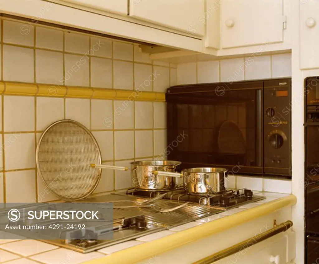 Close-up of stainless steel pans on gas hob beside wall-mounted microwave oven