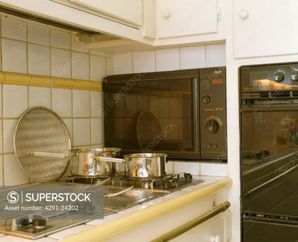 Stainless steel saucepans on steel hob beside built-in microwave and oven