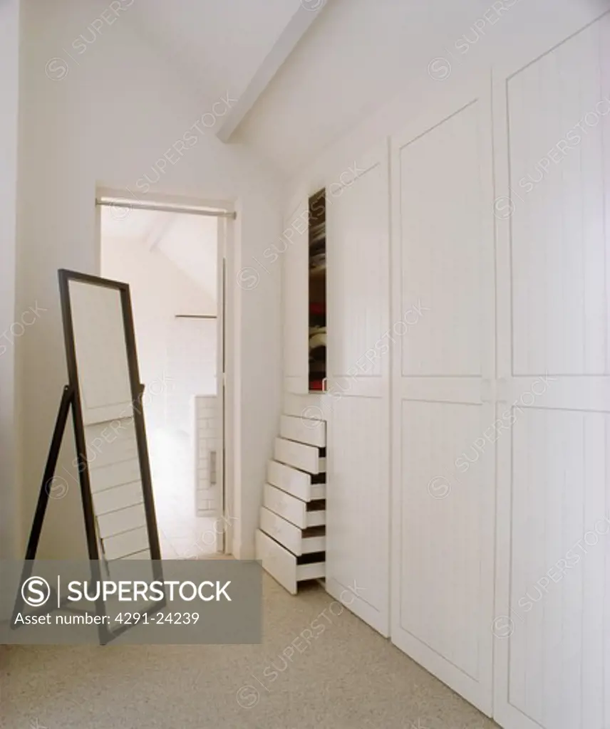 Tall freestanding mirror in modern white dressing room with fitted wardrobe