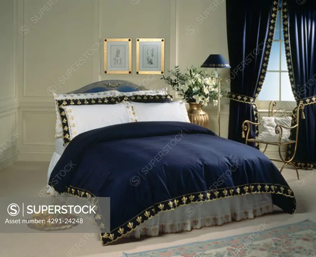 Bed with white pillows and gold-trimmed dark blue throw with matching curtains at window in traditional bedroom