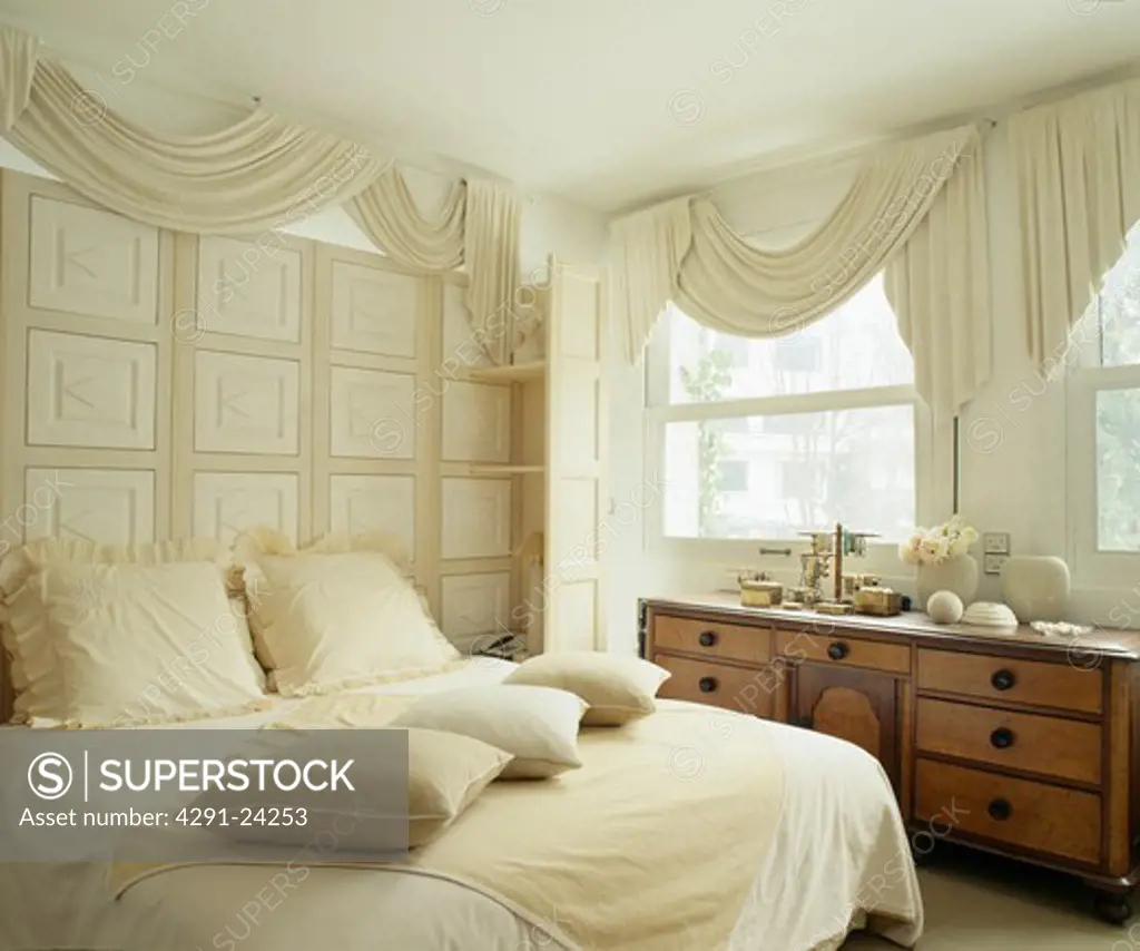 Cream drapes and cream panelling above bed with cream cushions and linen in traditional bedroom