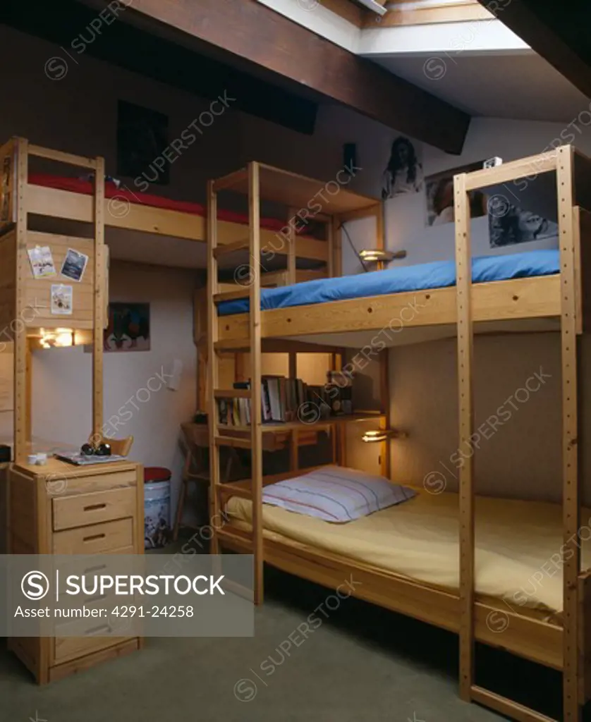Triple wooden bunk beds with wooden ladder in children's attic bedroom with narrow pine chest-of-drawers
