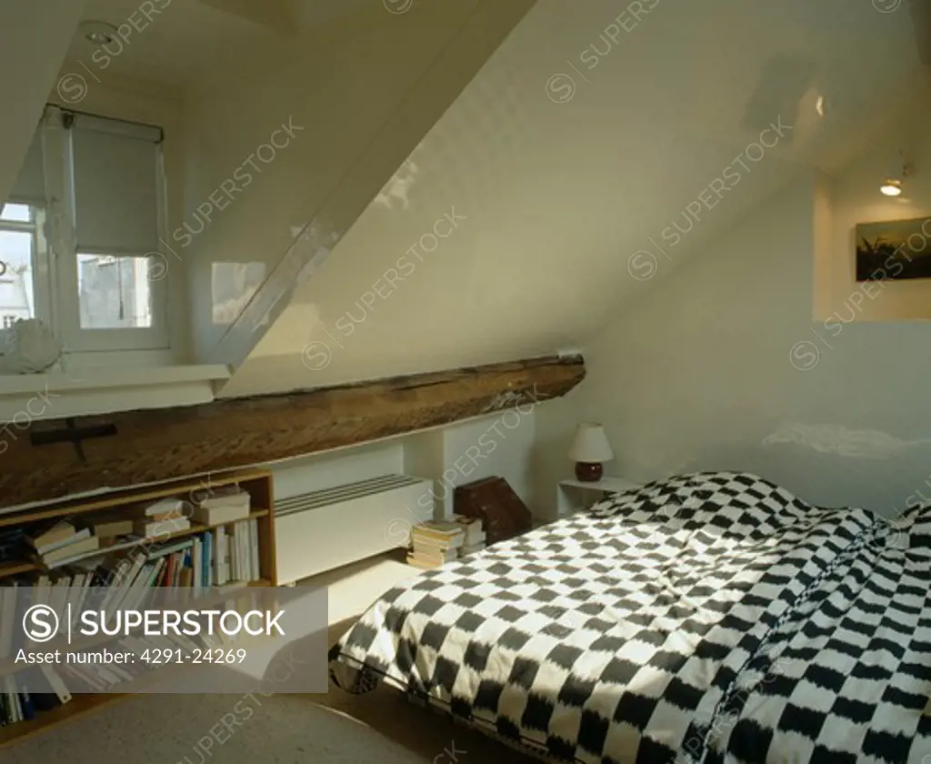 Black and white checked bedlinen on bed in attic bedroom with shelves below small dormer window