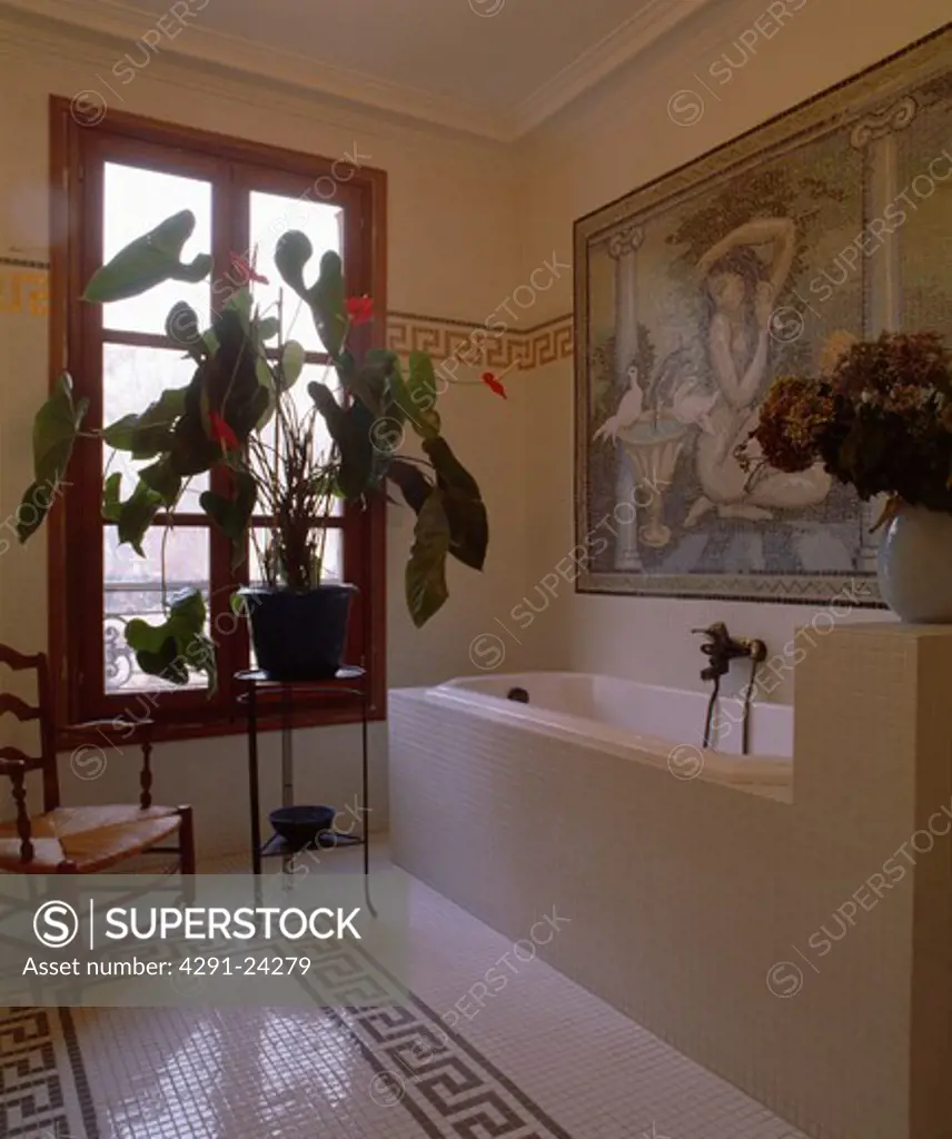 Large houseplant on table in front of window in bathroom with black and white tiled floor and mosaic picture above bath
