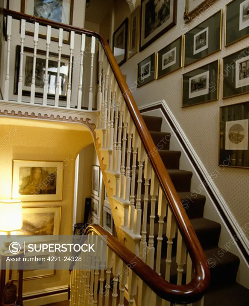 Group of pictures on wall above Victorian staircase with white bannisters and mahogany handrail