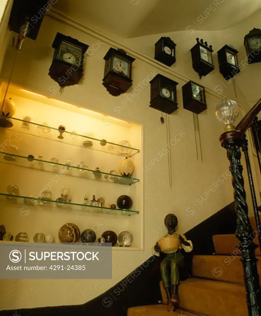 Collection of old clocks on wall with glass shelves in alcove above staircase with thirties figure
